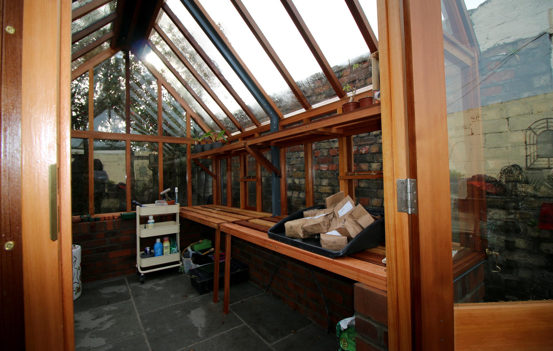 The spacious interior with optional cedar Staging & Shelving of the RHS Hyde Hall Victorian Greenhouse  installation in Rathgar, Dublin 6 with grey limestone patio & paving, retaining walls finished in red brick |  Owen Chubb Garden Landscapers